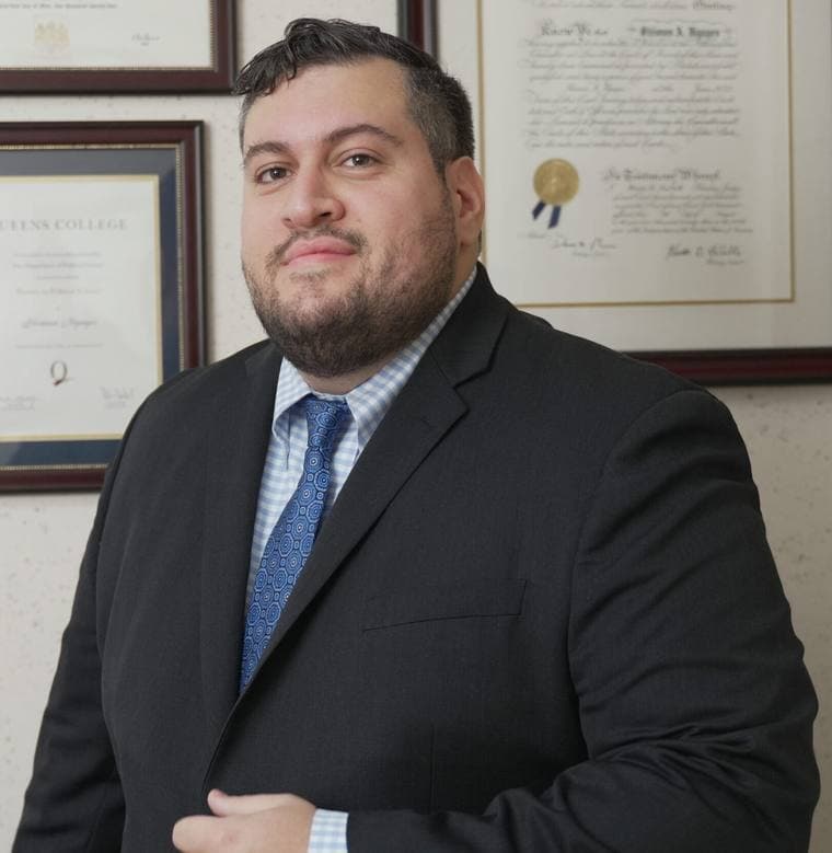 Shimun A. Ilyayev, Esq. in his Bayside office, with his Queens College diploma and New York bar admission certificate